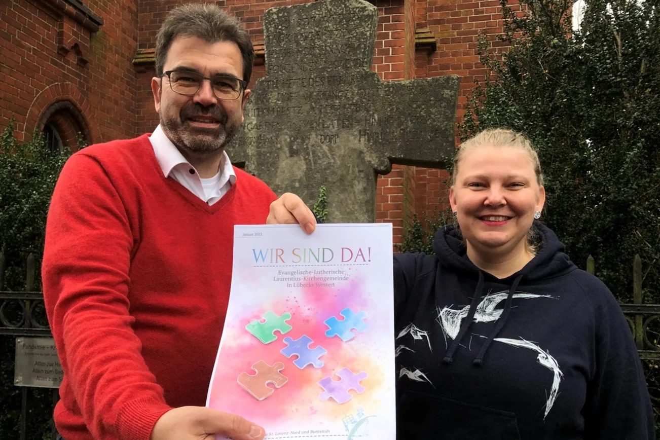 Ein Mann und eine Frau halten das Titelbild des Laurentius-Magazins in die Kamera. Darauf steht. Wir sind da. Das Bild zeigt bunte Puzzleteile vor einem roten Hintergrund.