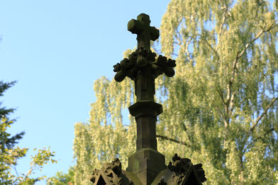 Ein Steinkreuz ragt in die Höhe. Im Hintergrund sieht man eine große Birke mit grünen Blättern. - Copyright: Ev.-Luth. Kirchenkreis Lübeck-Lauenburg