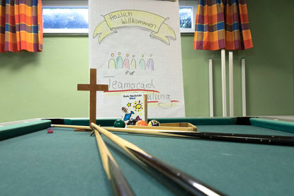 Billiardtisch mit Koes - Im Hintergrund ein braunes Holzkreuz - Copyright: Anja Sabrina Hagge