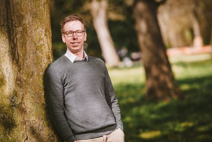 Junger Mann lächelt an einen Baum gelehnt in die Kamera. - Copyright: Guido Kollmeier