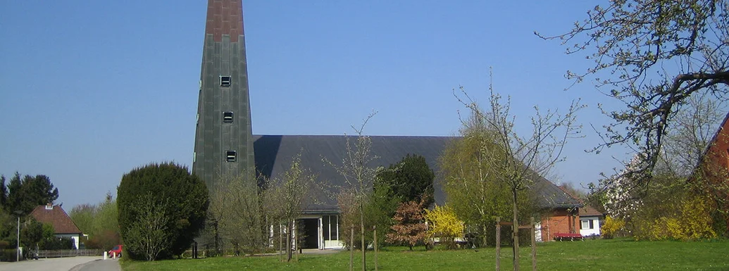 Außenansicht der Paul-Gerhardt-Kirche mit umliegenden Bäumen und Wiese
